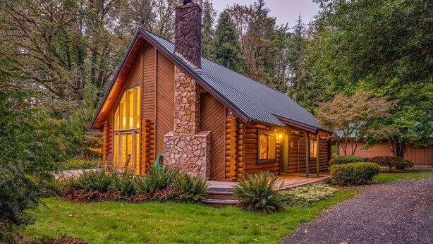 A log cabin with a stone chimney, a porch with seating, and a gravel driveway. - Awesome Log Cabin and Guest Home on Two Acres, Pet Friendly, Hot Tub, Patio,15 Miles to Mt. Hood (Brightwood)