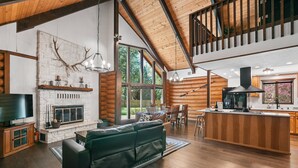 A spacious log cabin interior with a fireplace, a large sofa, wooden floors, and a kitchen area. - Awesome Log Cabin and Guest Home on Two Acres, Pet Friendly, Hot Tub, Patio,15 Miles to Mt. Hood (Brightwood)