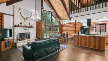 Un intérieur spacieux de chalet en bois, avec une cheminée, un grand canapé, des planchers en bois et un coin cuisine.