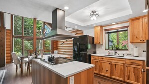 A modern kitchen with wooden cabinets, a large island, and a view of the outdoors. - Awesome Log Cabin and Guest Home on Two Acres, Pet Friendly, Hot Tub, Patio,15 Miles to Mt. Hood (Brightwood)