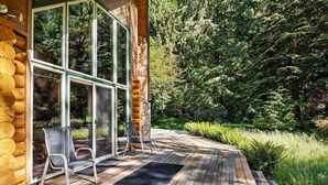 A wooden deck with two chairs, a stone wall, and a glass door leading to a forested area. - Awesome Log Cabin and Guest Home on Two Acres, Pet Friendly, Hot Tub, Patio,15 Miles to Mt. Hood (Brightwood)