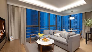 A modern living room with a grey sofa, a round coffee table with fruit, and a large window with a city view.