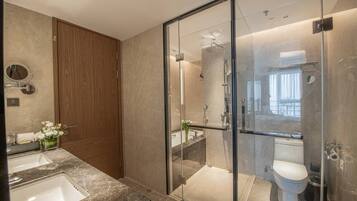 Un baño moderno con ducha envuelta en vidrio, tocador doble y puerta de madera.