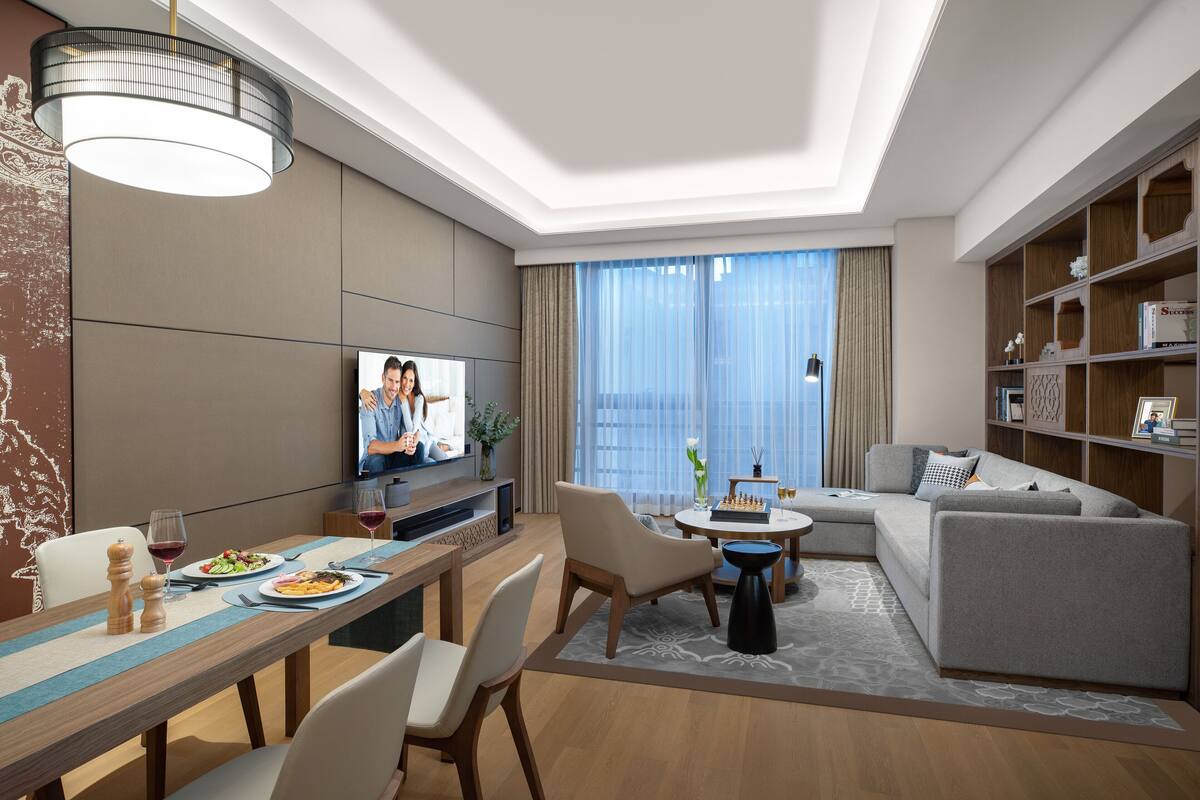 A modern living room with a dining area, a sofa, a television, and a bookshelf.