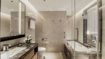 A modern bathroom with a glass shower enclosure, a large mirror, a marble countertop, and a toilet.