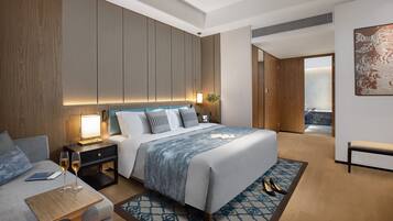 Una habitación de hotel moderna con una cama grande, una mesita de noche con lámpara, un área de descanso y vistas a un balcón.