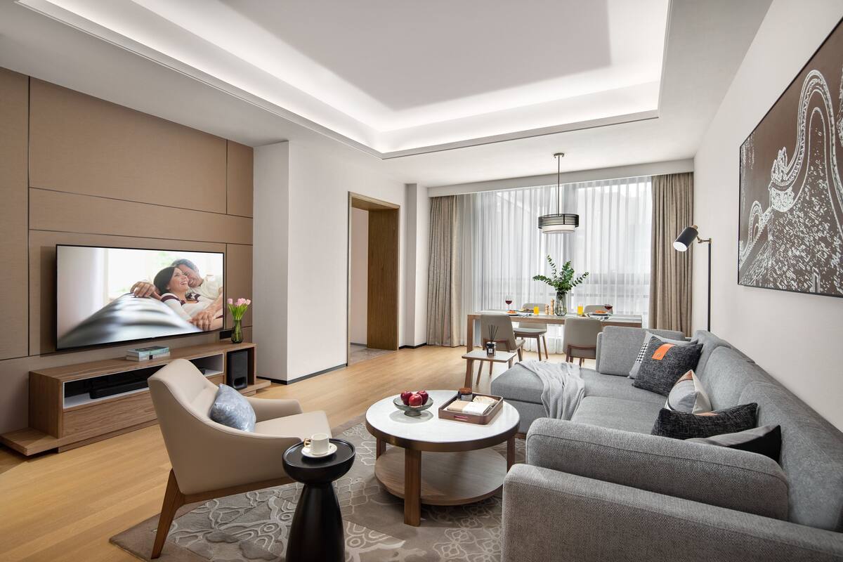 A modern living room with a flat-screen TV, a sofa, a coffee table, and a dining area with a table and chairs.