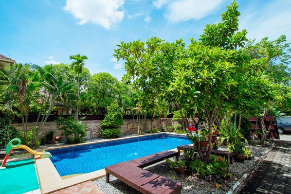 A swimming pool surrounded by lush greenery, a wooden deck, and a stone wall.