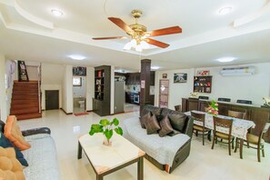 A spacious living area with a ceiling fan, a sofa, a dining table with chairs, and a kitchen in the background.