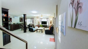 Amplia sala de estar con sofá, mesa de centro y televisor. Se observan estanterías y una escalera que conduce a otro nivel.