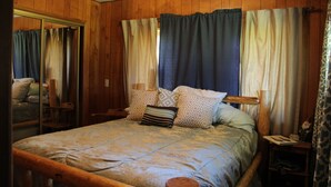Een slaapkamer met houten lambrisering, een bed, kussens, een nachtkastje en een spiegel.