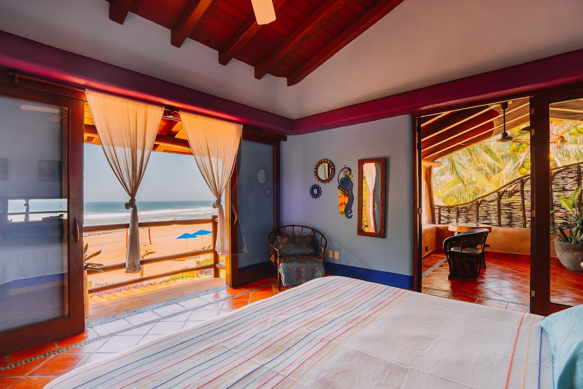A bedroom with a large bed, a view of the beach, and a balcony with a chair.