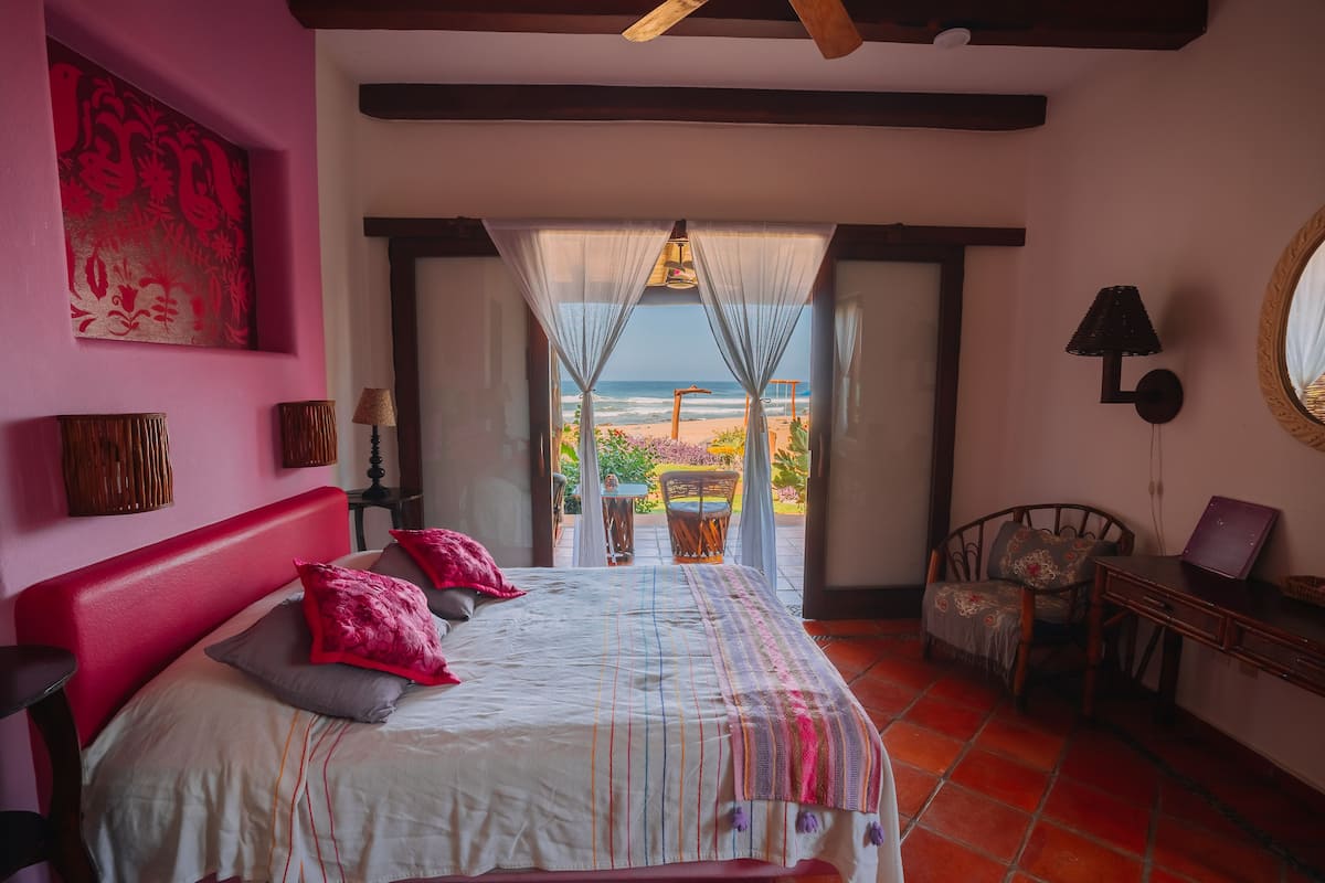A bedroom with a large bed, a view of the beach, and a dining area with a table and chairs.