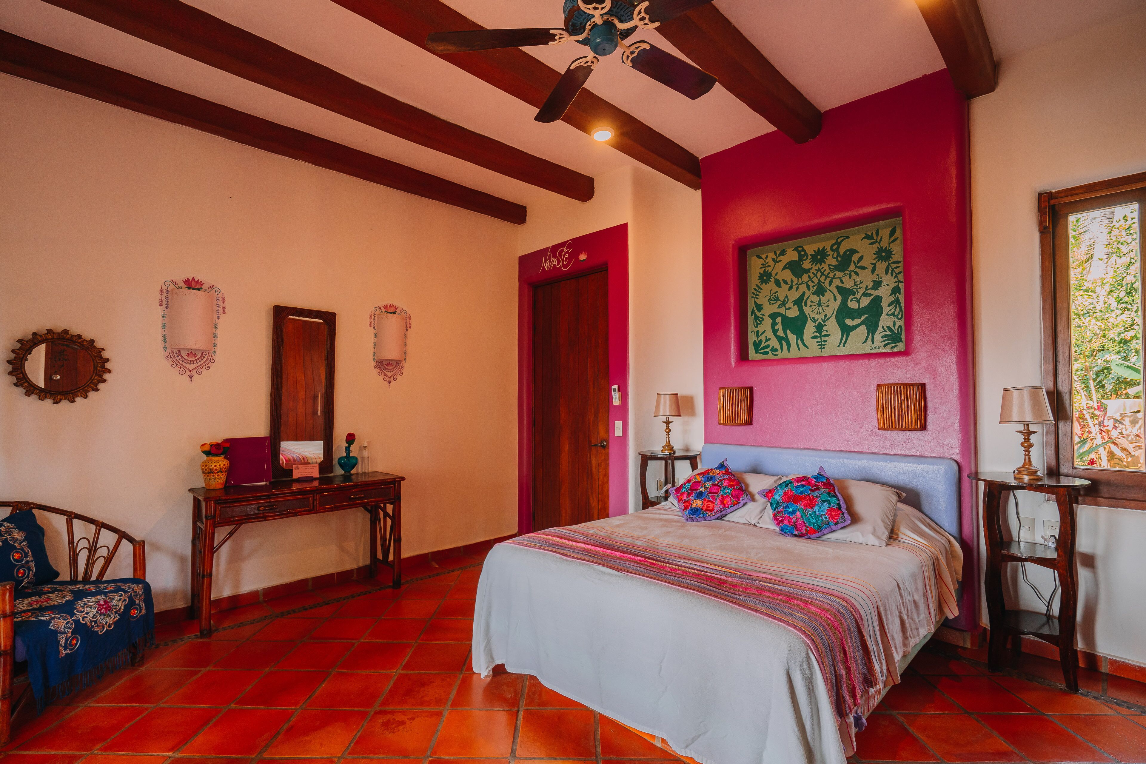 A bedroom with a bed, wooden furniture, a ceiling fan, a red door, and a window.