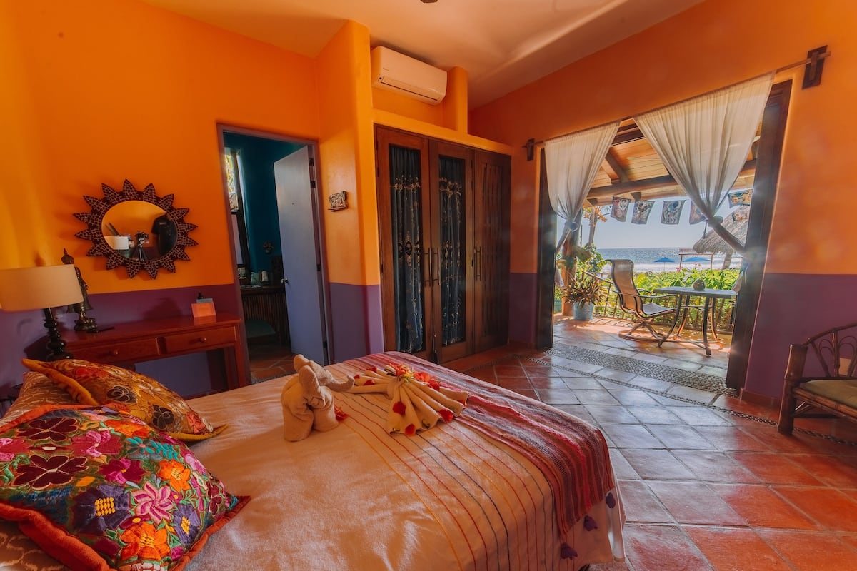 A hotel room with a bed, a nightstand, a mirror, and a view of the beach through the balcony doors.