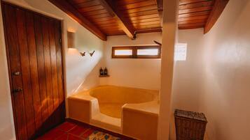 Un baño con puerta de madera, una bañera, una cesta de mimbre y un felpudo.