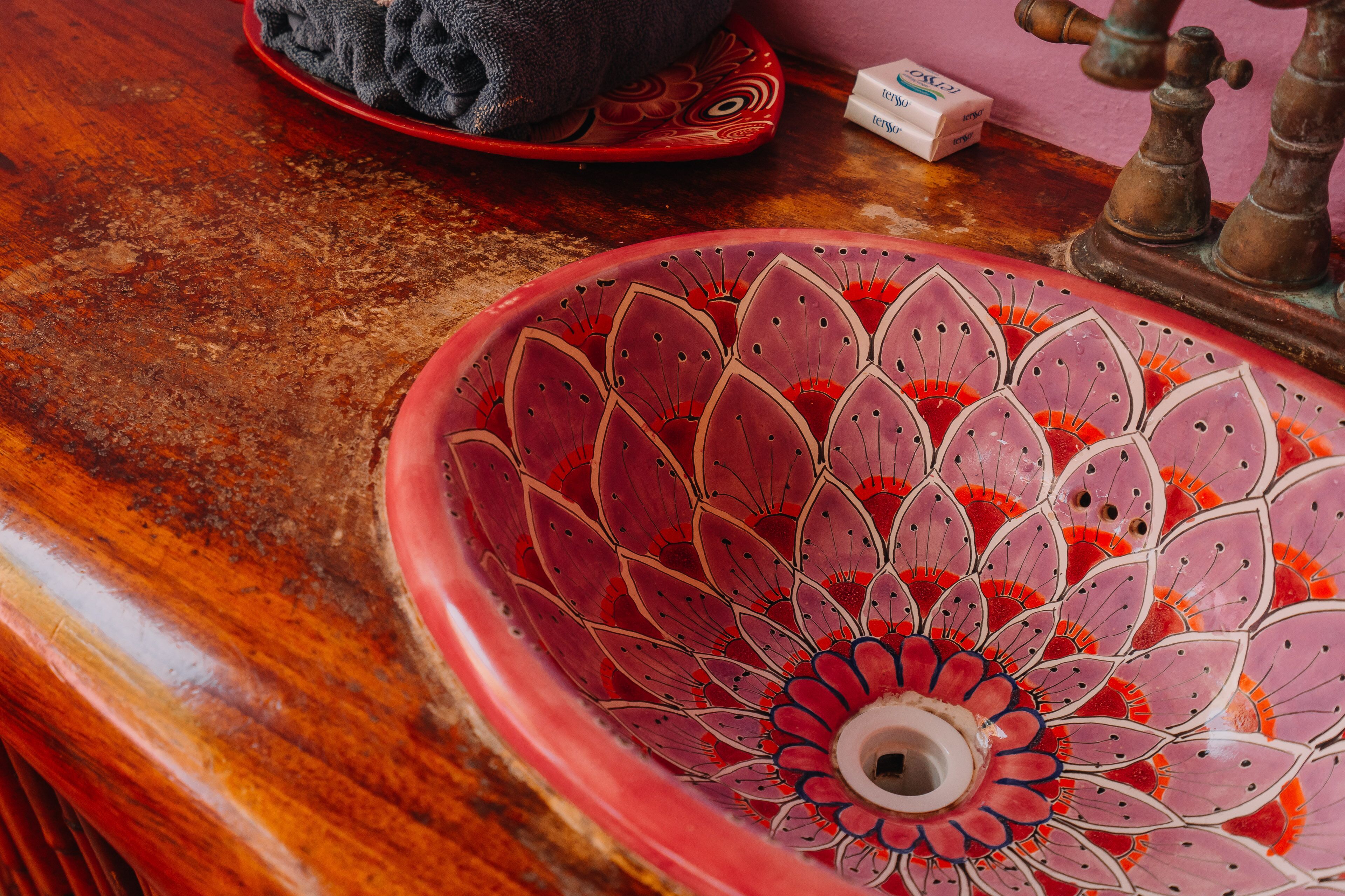 Un lavabo de cerámica rojo con motivos florales, un plato rojo con diseño decorativo y un grifo antiguo sobre una superficie de madera.