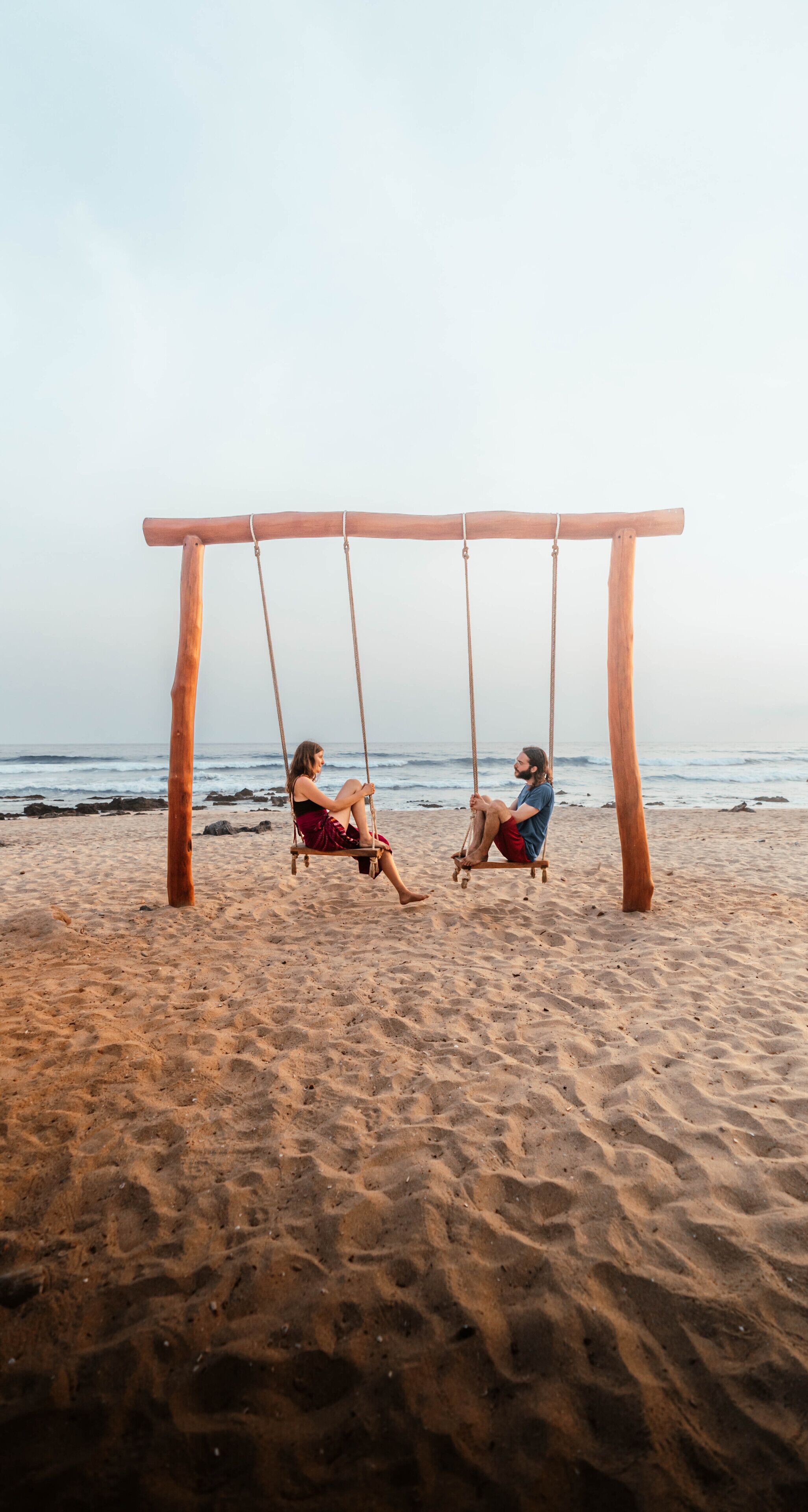 A wooden swing set on a sandy beach with the ocean in the background.