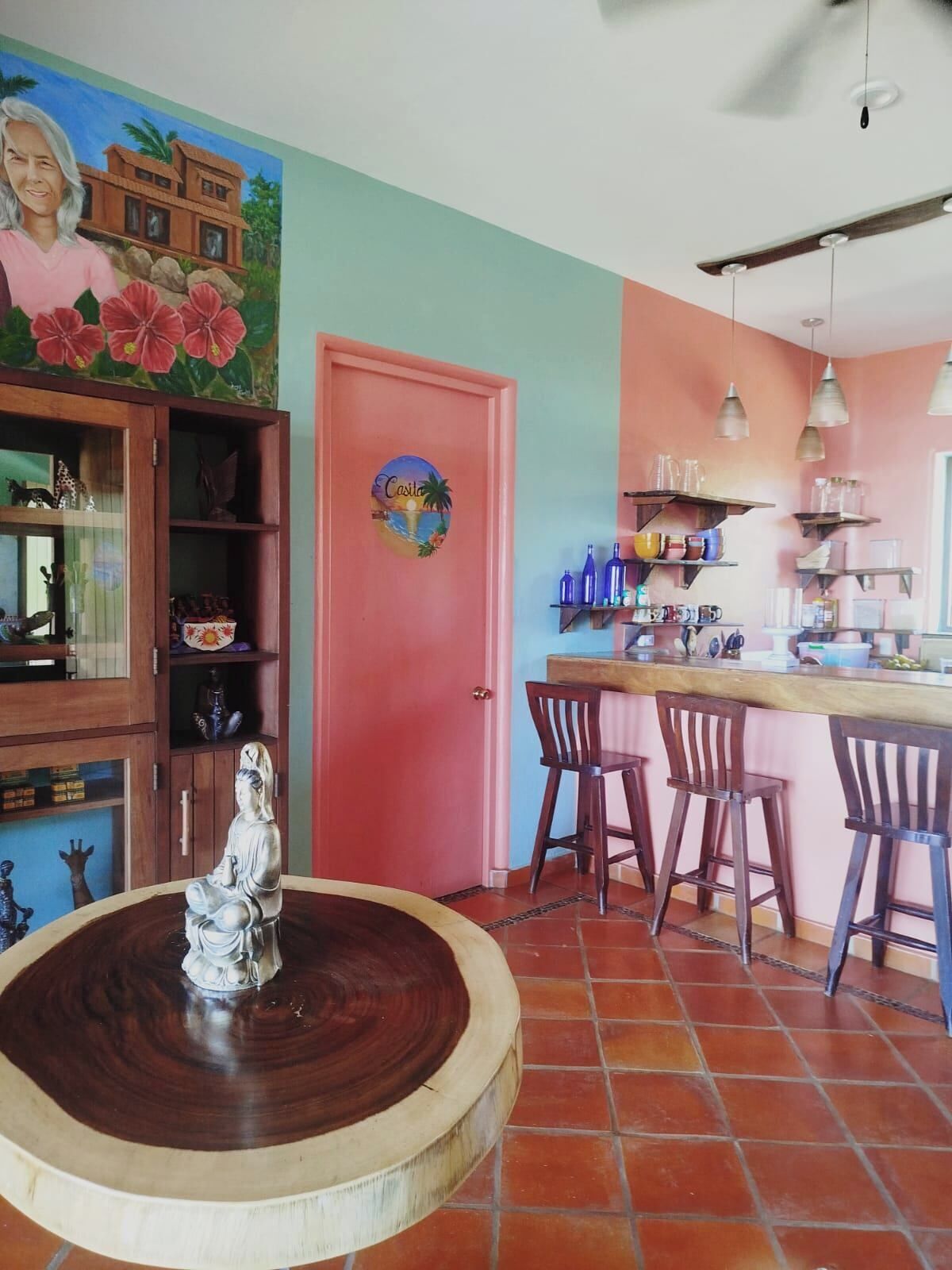 A kitchen with a red door, a statue on a wooden table, and a mural on the wall.