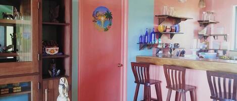 A kitchen with a red door, a statue on a wooden table, and a mural on the wall.