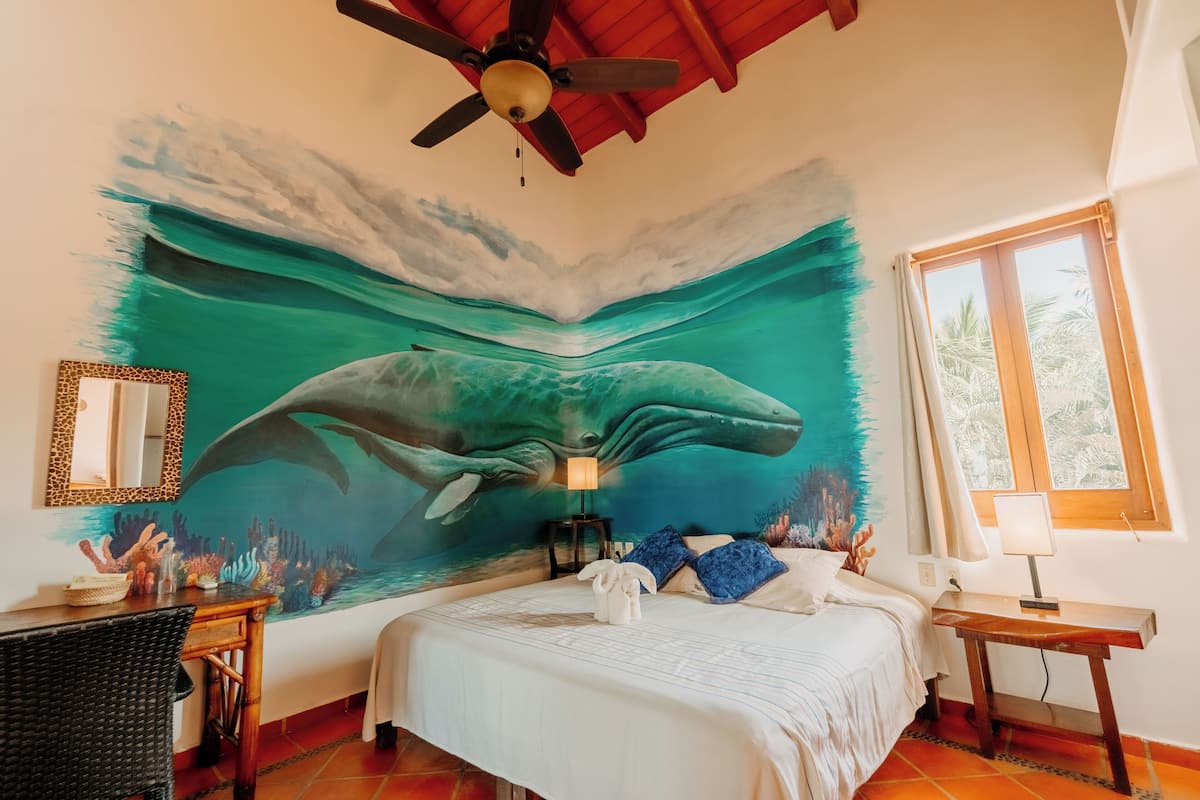 A bedroom with a mural of a whale, a bed, a desk, and a window.