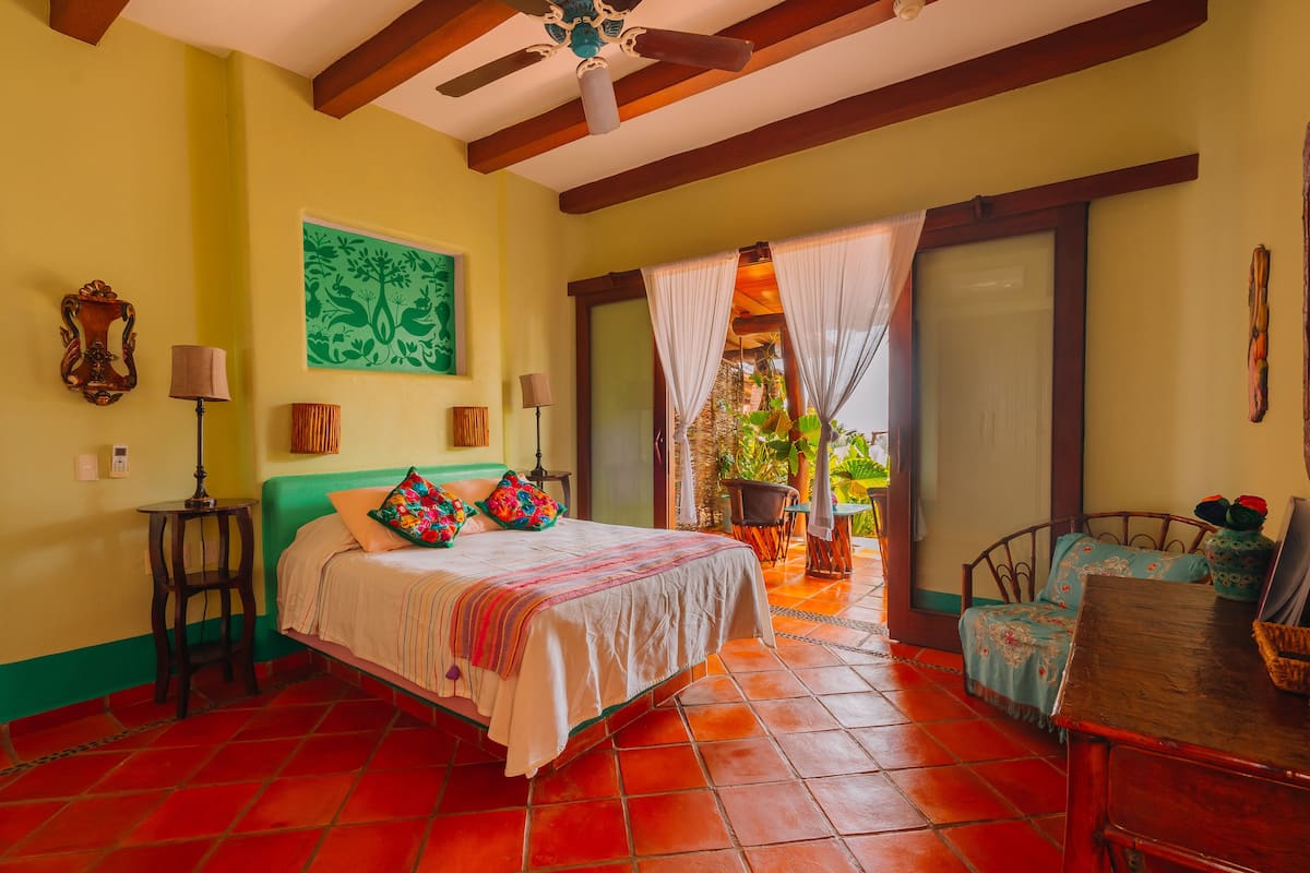 A bedroom with a bed, a chair, a table, and a ceiling fan.