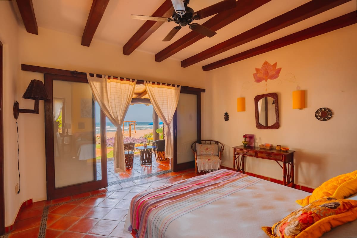 A bedroom with a bed, a chair, a table, and a view of the beach.