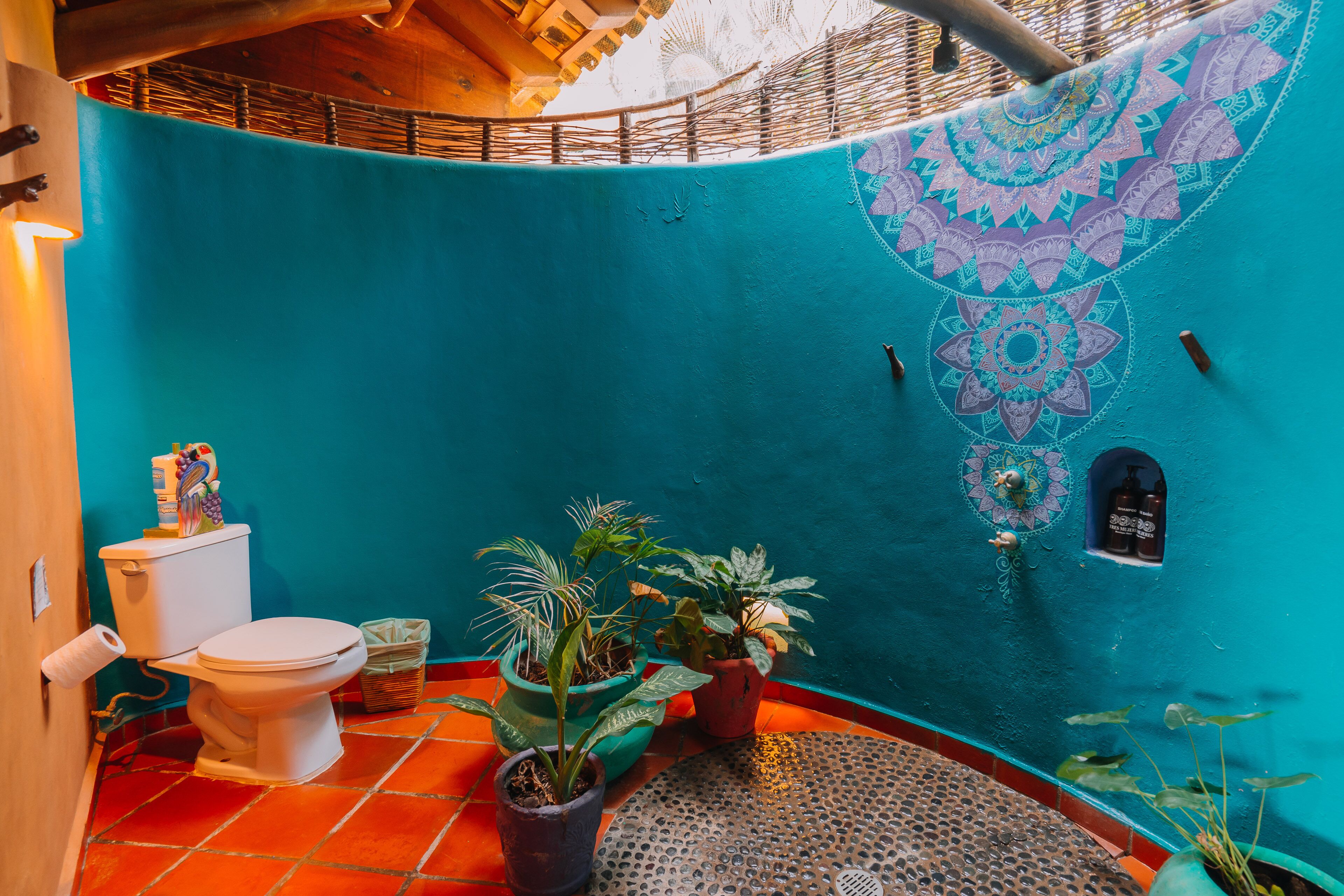 Un baño con inodoro, tres plantas en macetas, lavamanos y una pared decorativa con diseño geométrico.