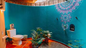 Un baño con inodoro, tres plantas en macetas, lavamanos y una pared decorativa con diseño geométrico.
