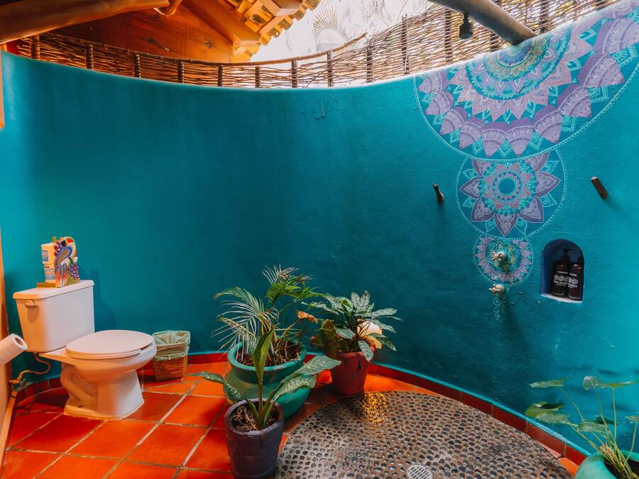 Un baño con inodoro, tres plantas en macetas, lavamanos y una pared decorativa con diseño geométrico.