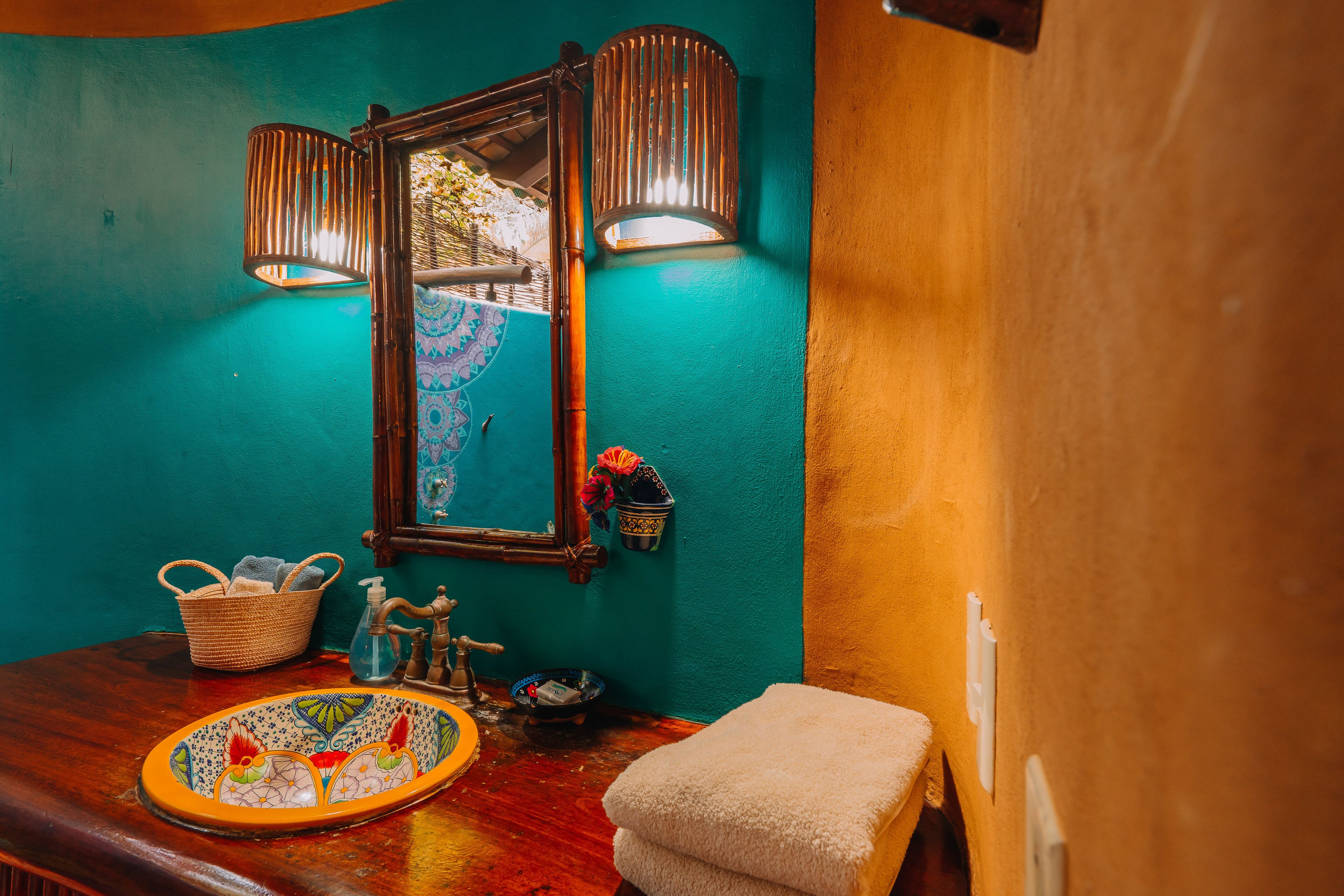 A bathroom with a wooden vanity, a mirror, two wall-mounted lights, a sink with a decorative tile backsplash, a towel, and a basket with towels.