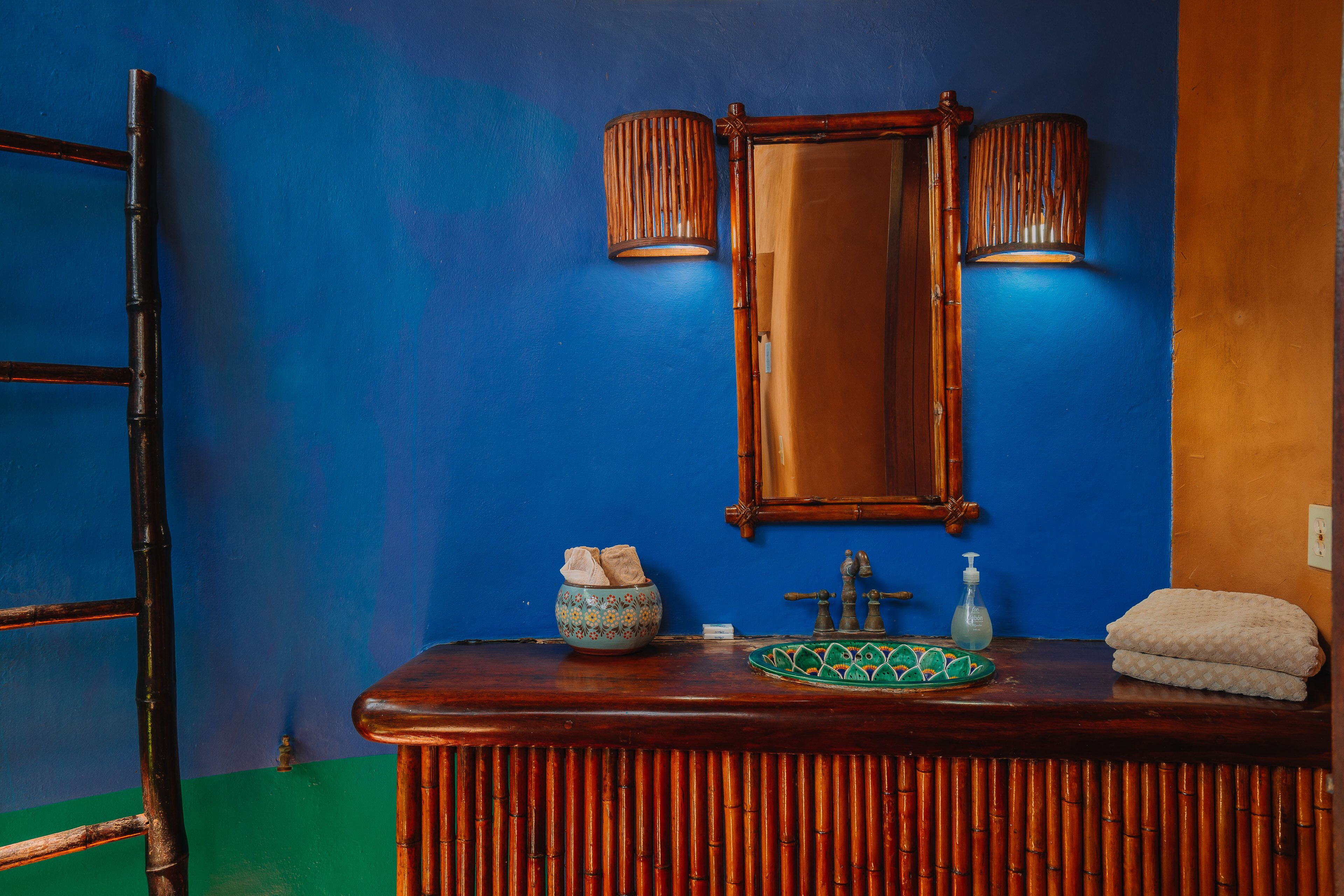 A bathroom with a wooden vanity, a mirror, two wall-mounted lights, a towel, a soap dispenser, and a decorative bowl.