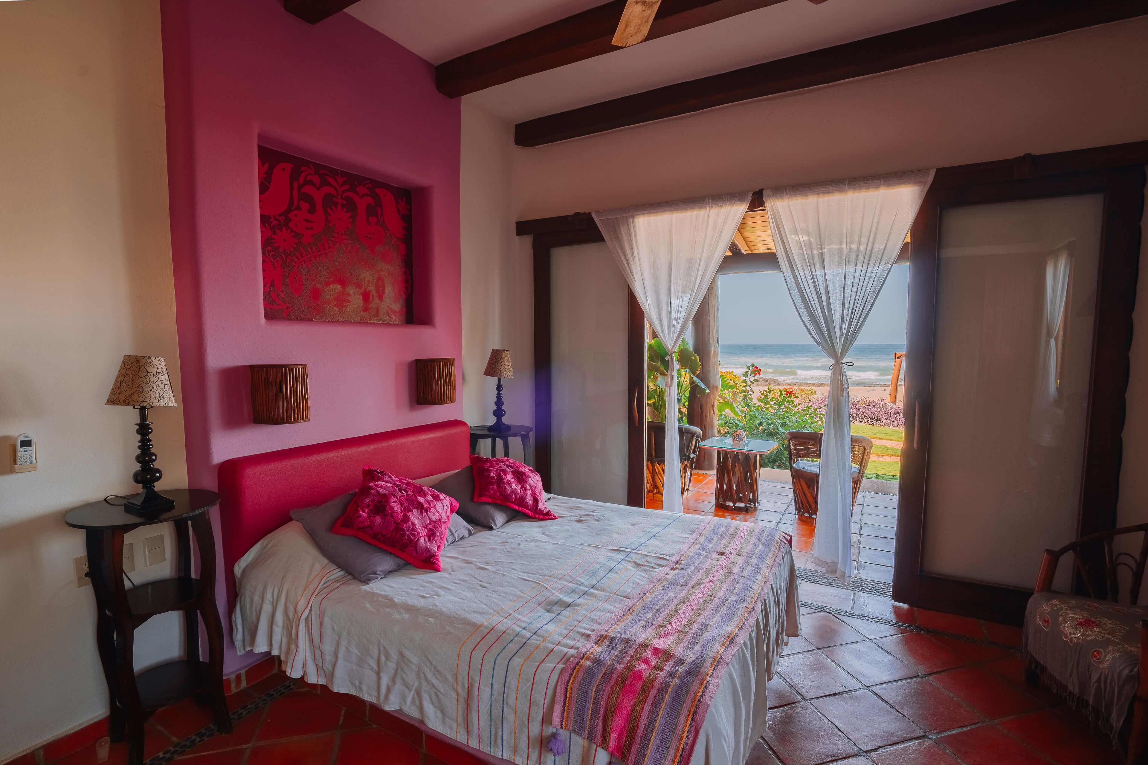 Une chambre avec un grand lit, un mur rose et une vue sur l’océan.