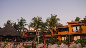 Un resort con estructuras de techo de paja, palmeras y un área de piscina.