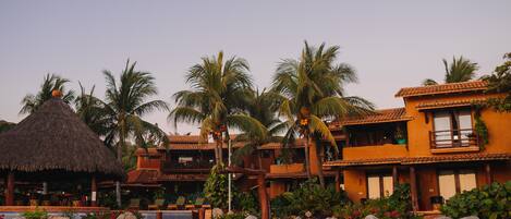A resort with thatched-roof structures, palm trees, and a pool area.