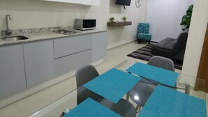 A modern kitchen with white cabinets, a microwave, and a sink. There is a dining area with a glass table and blue placemats. A flat-screen TV is mounted on the wall, and a small plant is on a shelf. - beautiful loft ,two blocks from the beach , walk or ride a bike and explore  mzt (Mazatlán)