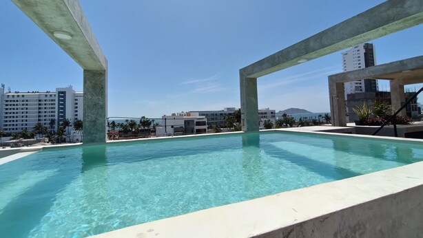 A swimming pool with clear blue water, surrounded by concrete structures and buildings in the background. - beautiful loft ,two blocks from the beach , walk or ride a bike and explore  mzt (Mazatlán)