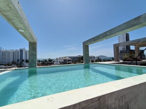 A swimming pool with clear blue water, surrounded by concrete structures and buildings in the background.