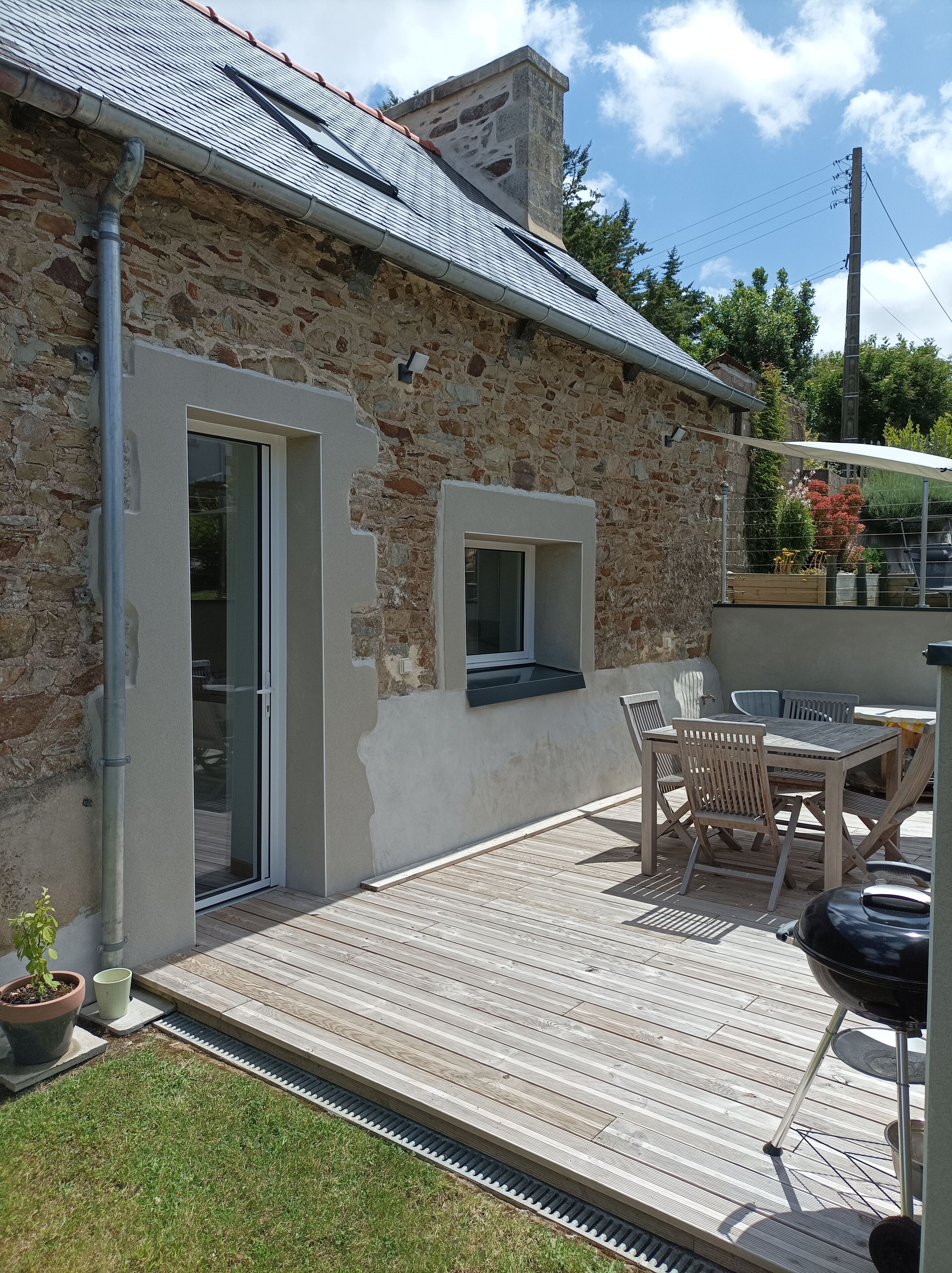Une maison en pierre avec une terrasse en bois, une porte-fenêtre coulissante et une petite fenêtre.