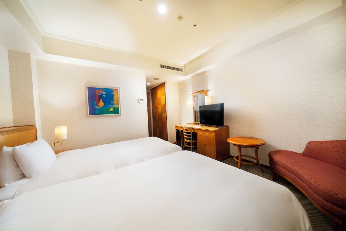 Une chambre d’hôtel avec deux lits, un bureau avec une télévision, une petite table et un canapé rouge.