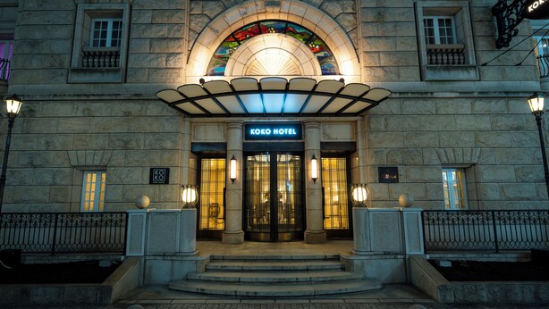 Der Eingang des Koko Hotels mit einer Stein-Fassade, Bogenfenstern und einem Schild über den Türen.