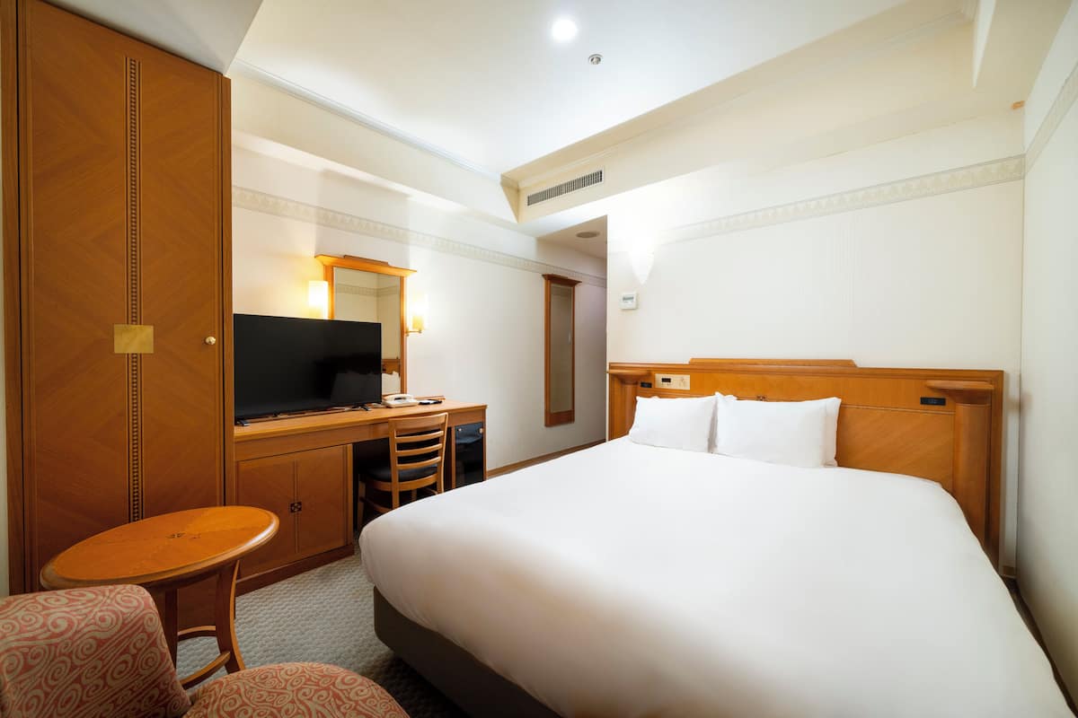 Une chambre d’hôtel avec un grand lit, un bureau avec une télévision, un miroir et une petite table.