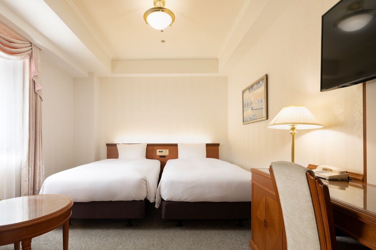 Quarto de hotel com cama, mesas de cabeceira, uma cadeira, televisão e abajur.