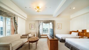 Ein Hotelzimmer mit einer Couch, einem Schreibtisch, zwei Betten, einem Fernseher und einem Fenster mit Vorhängen.