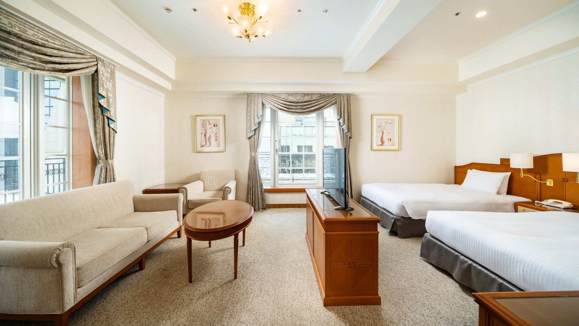 A hotel room with a sofa, two armchairs, a coffee table, a TV, a bed, and a desk.