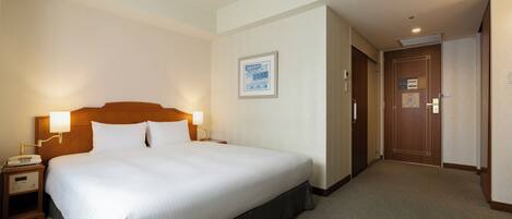 A hotel room with a large bed, bedside lamps, a framed picture on the wall, and a door to the right.