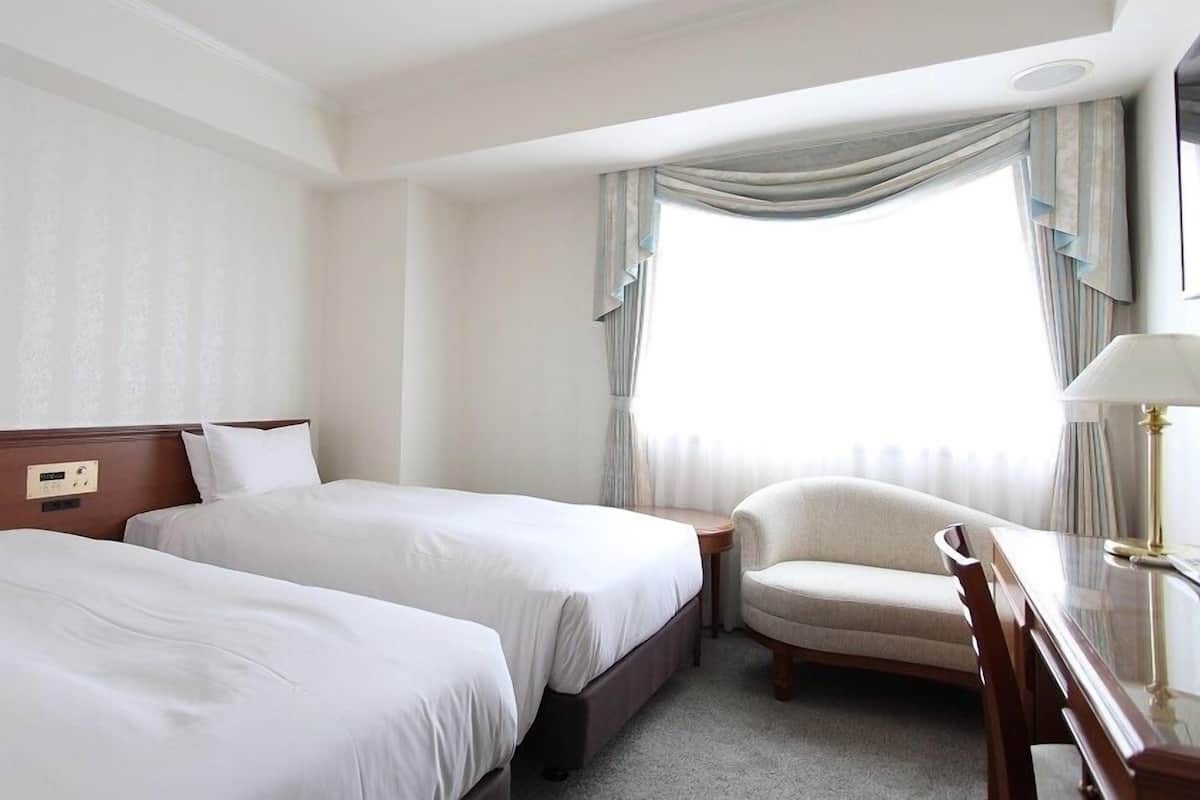 Une chambre d’hôtel avec deux lits, une chaise, un bureau et une fenêtre avec des rideaux.