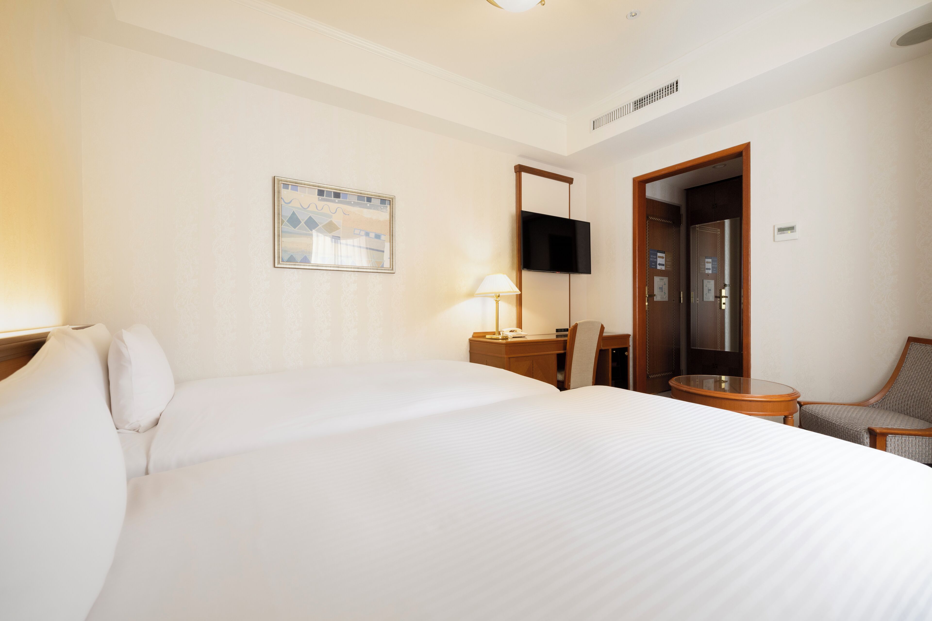 A hotel room with a large bed, a desk with a chair, a television mounted on the wall, and a door leading to another room.