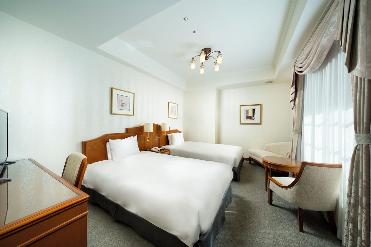 Une chambre d’hôtel avec deux lits, un bureau, une chaise et une petite table.
