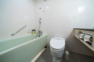 A bathroom with a bathtub, toilet, and a handrail.